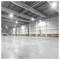 Empty warehouse interior with high ceilings, bright overhead lights, concrete floor, and a forklift near the far left wall.