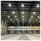 Empty warehouse interior with a high metal roof, bright ceiling lights, concrete floor, and loading bay doors along the back wall.