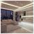 Modern open-plan living room and kitchen at night with beige sectional sofa, city skyline through large windows, and sleek illuminated cabinets and island.