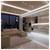 Modern open-plan living room and kitchen at night, with beige sectional sofa, glossy white floor, recessed lighting, and city skyline visible through large windows.