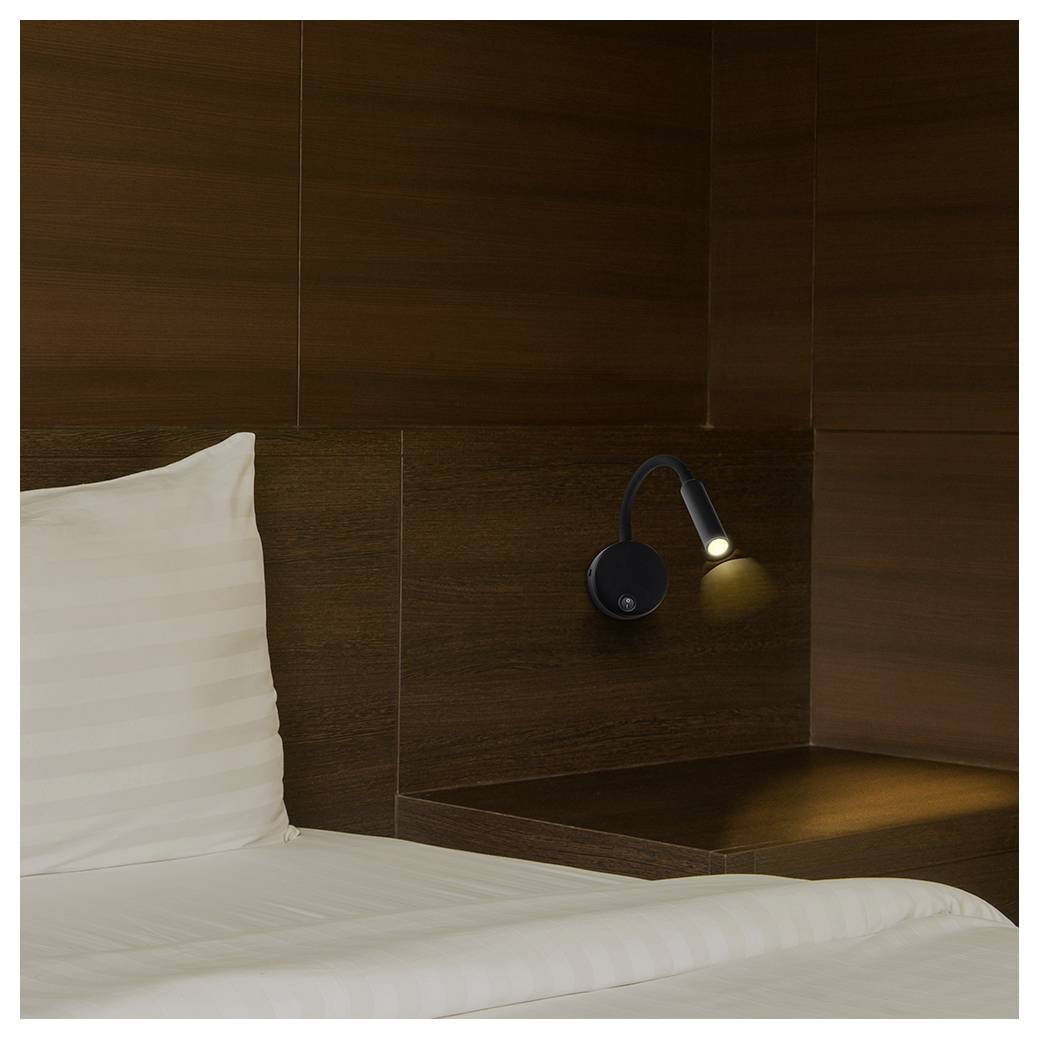 A neatly made white bed beside a dark wood headboard with a small lit reading lamp, suggesting a cozy hotel-style bedroom.<br>