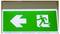 Green emergency exit sign with a white left arrow and running person icon, indicating the exit route is to the left.