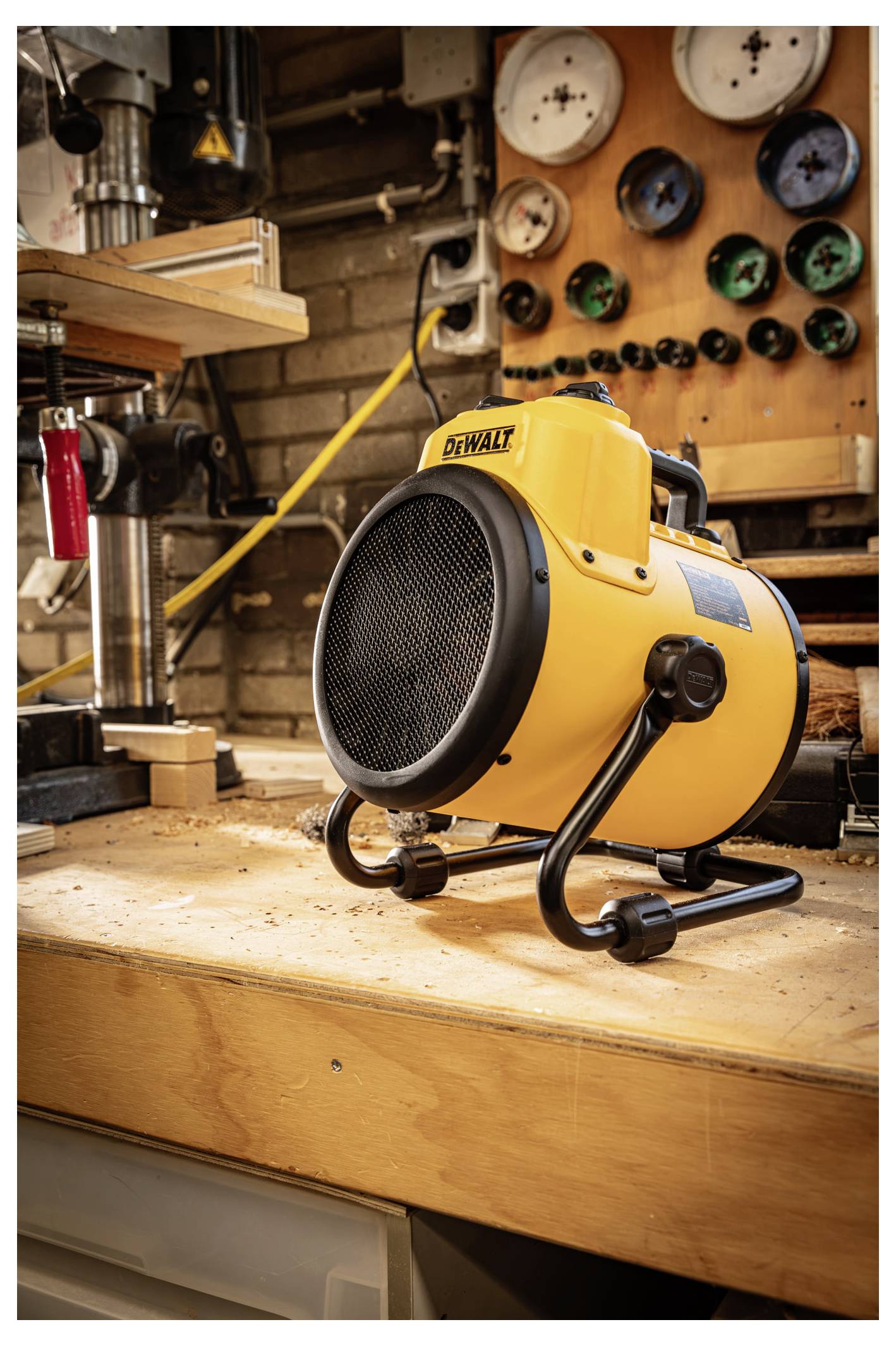 Yellow DeWalt portable electric heater on a workbench in a workshop, with gauges and tools in the background.
