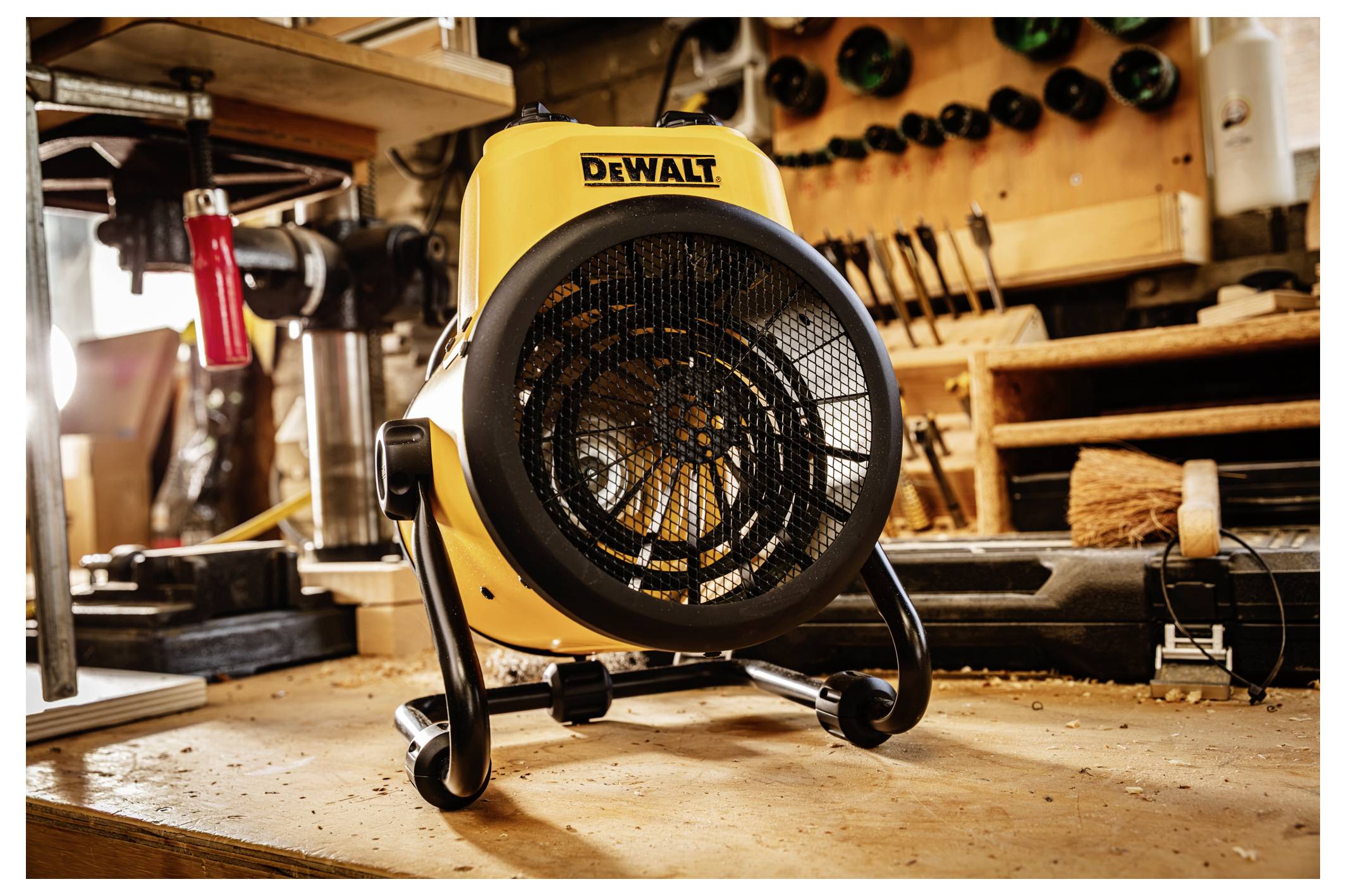 Yellow DEWALT portable fan on a workshop floor, aimed forward with tools and wooden shelves in the background.<br>