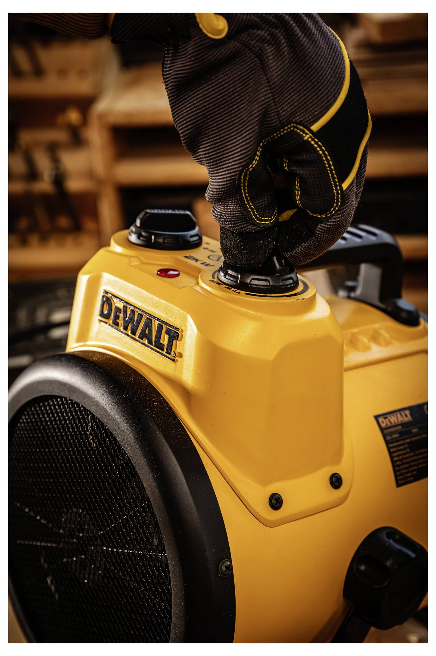 Gloved hand presses the control on a yellow DEWALT portable heater or fan with a large black grille.<br>