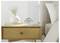 A bedside table with a white vase of flowers, stacked books, and a small analog alarm clock beside a bed.<br>