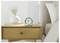 Bedroom nightstand with a small green alarm clock, vase of flowers, and books beside a bed with white pillows.