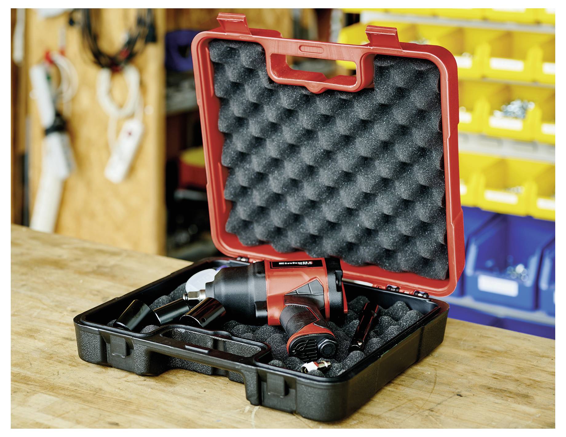 Cordless power drill in an open black carrying case on a workbench, with foam lining and workshop storage in the background.