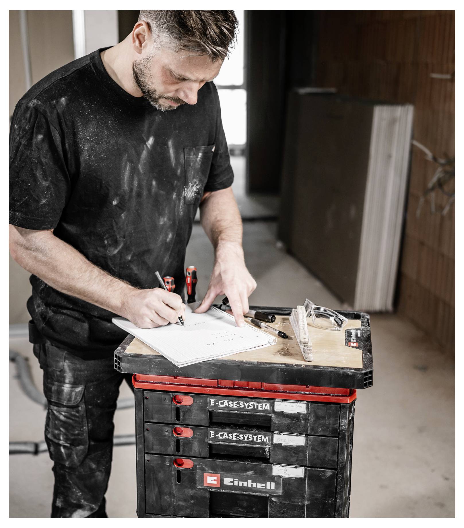Man taking measurements and notes on a clipboard beside a tool case in a renovation work area.