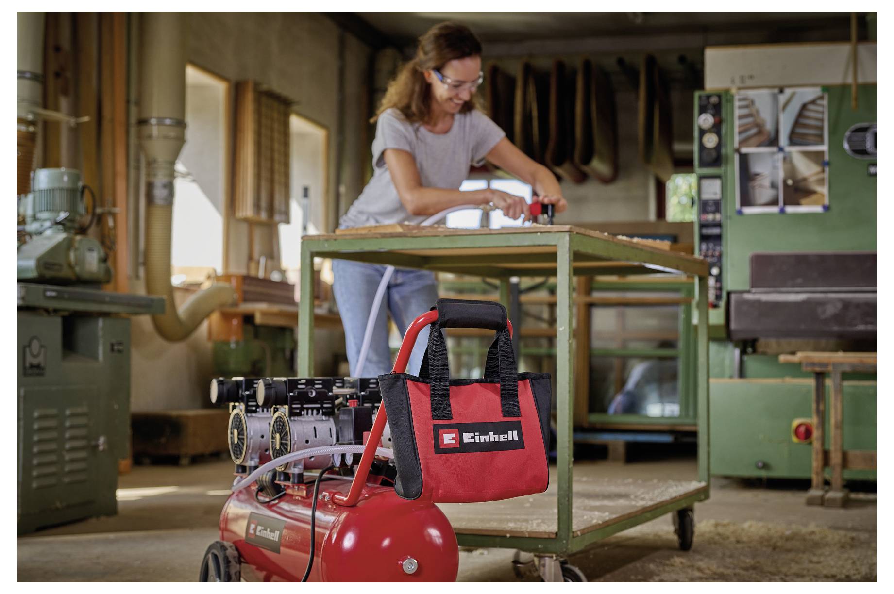 Woman sanding a wooden workbench in a workshop, with a red Einhell air compressor in the foreground.