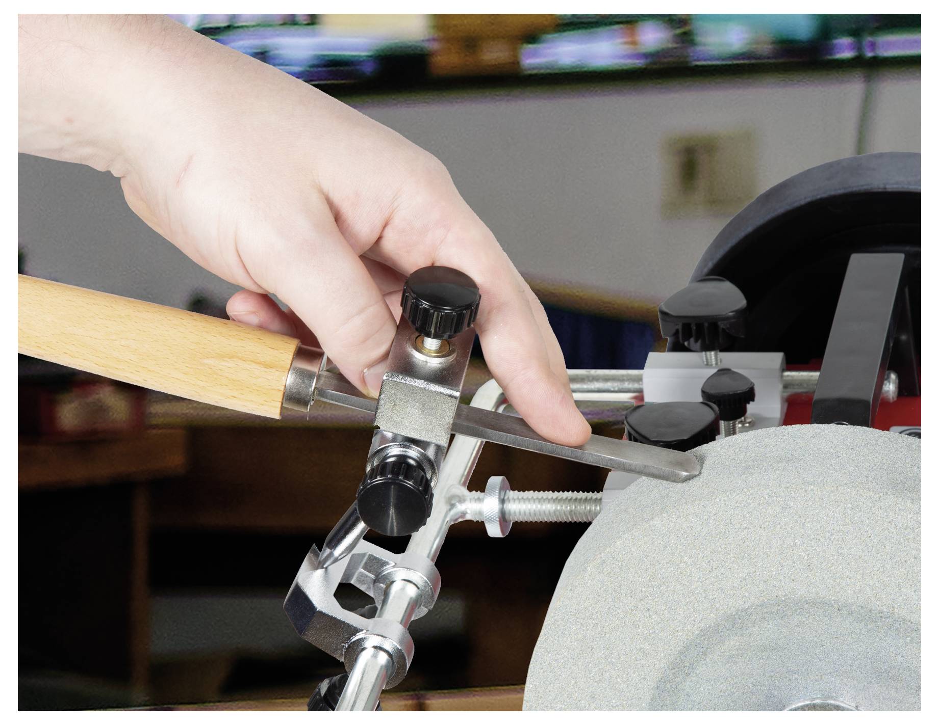 Close-up of a hand adjusting a knife sharpener against a grinding wheel on a workbench.