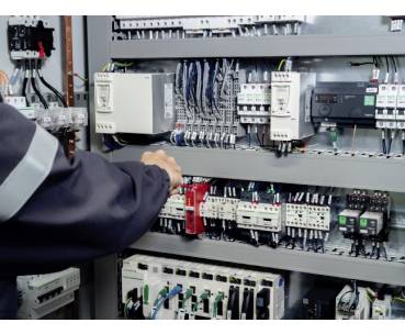 Technician inspecting an electrical control panel with wiring, relays, breakers, and industrial automation components.
