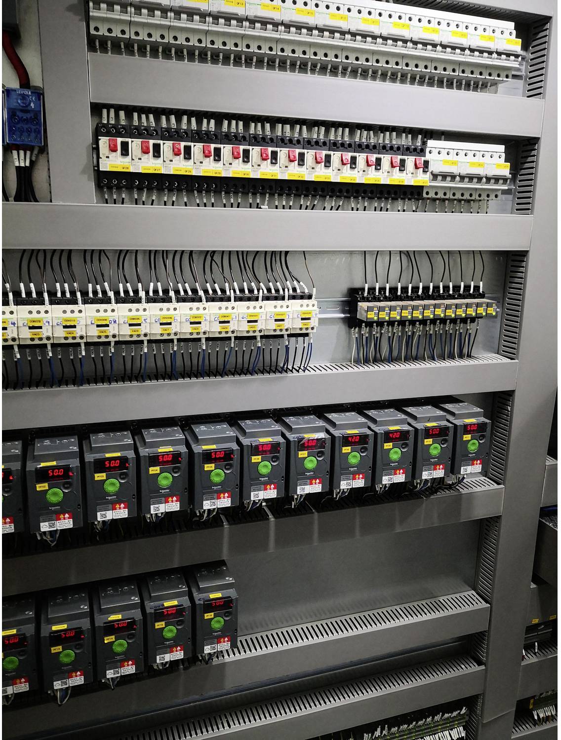 Electrical control cabinet with rows of circuit breakers, relays, and motor drives mounted on DIN rails, showing organized industrial wiring and power controls.