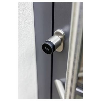 Close-up of a black cylindrical door lock or latch mounted on a dark metal door next to a silver handle.