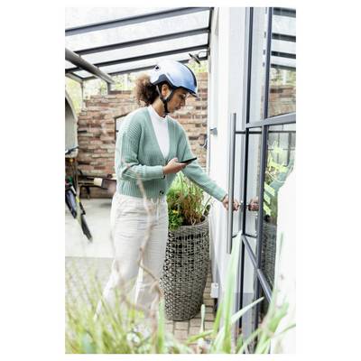 Woman in a blue helmet uses a smartphone while opening a glass door on a patio or balcony.