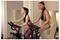 Two women exercising on stationary bikes in a gym studio, one in front and one behind, both leaning forward and pedaling.