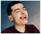 Smiling young man with eyes closed, tongue out, against a teal-to-gray studio background.