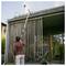 Person using an extended pole to clean the upper exterior of a modern house with vertical wooden slats and a patio area.