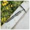 Handheld garden cultivator resting on a concrete edge beside yellow flowers and green foliage.