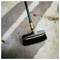 Black-and-orange push broom lying on a sunlit concrete surface with scattered dirt and leaves.