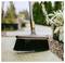 Outdoor broom with black bristles and orange accents sweeping a patio path beside plants and gravel.<br>