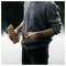 Person in a gray sweater holding a piece of wood and a knife, preparing to whittle or carve outdoors.<br>
