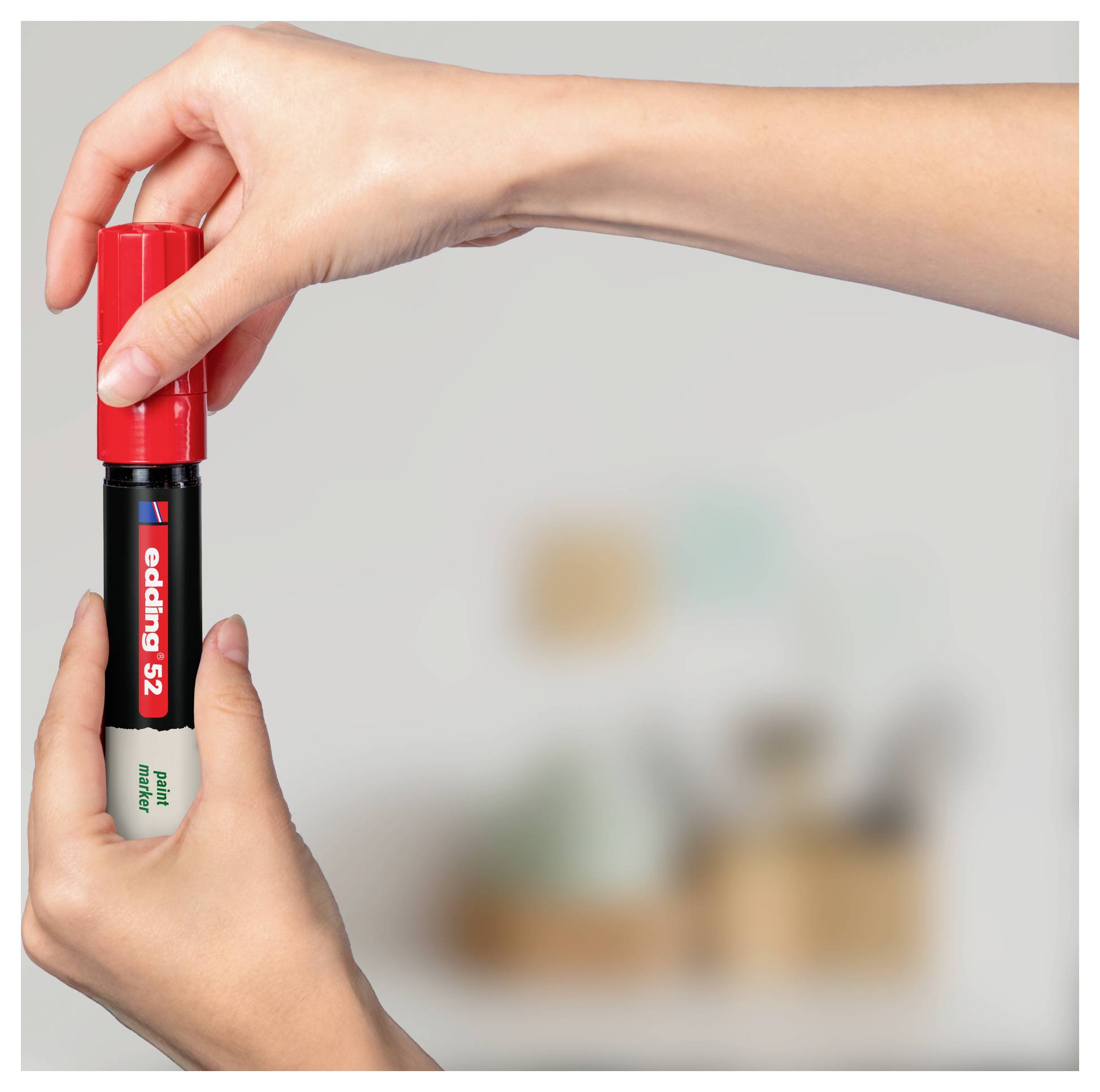 Hands holding a red and black Edding 52 marker upright against a blurred office background.