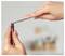 Hands use tweezers to remove a small red cap from a tube of glue or adhesive against a blurred background.