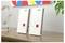 Two white FRITZ! devices standing on a wooden shelf beside a plant and glass award, with a colorful wall print above.