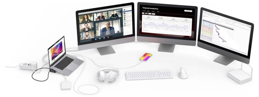 Multiple computer monitors display a video conference and analytics dashboards, connected to a laptop with headset, keyboard, mouse, and accessories on a desk.