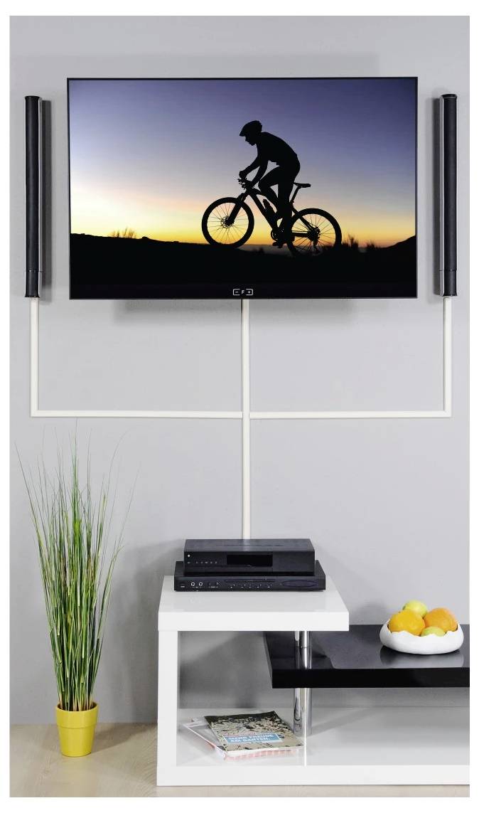 Flat-screen TV showing a silhouetted cyclist at sunset above a white media stand with speakers, a plant, and a bowl of oranges.