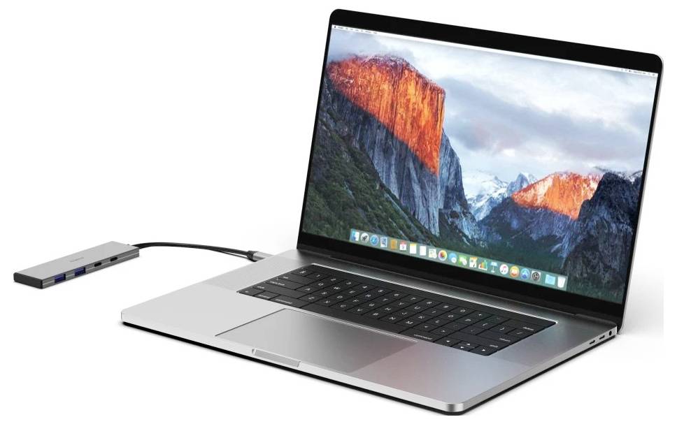 A silver laptop connected by cable to a slim USB hub, shown on a white background.