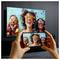 Hands holding a smartphone to mirror a colorful party image on a large TV screen, showing three laughing women with confetti and sunglasses.