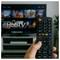 Hand holding a TV remote in front of a smart TV screen showing the HbbTV logo.