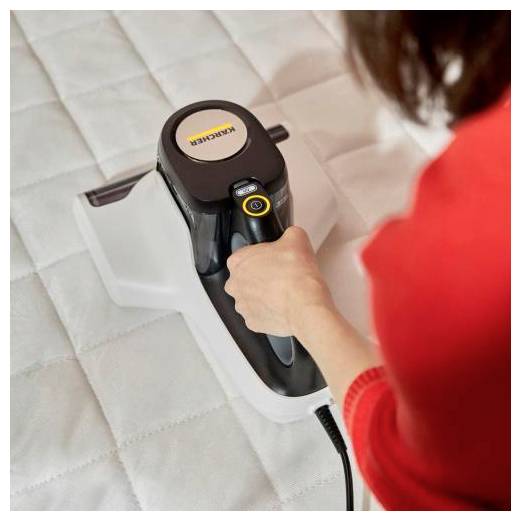 Person using a handheld steam cleaner to clean a mattress or padded surface.