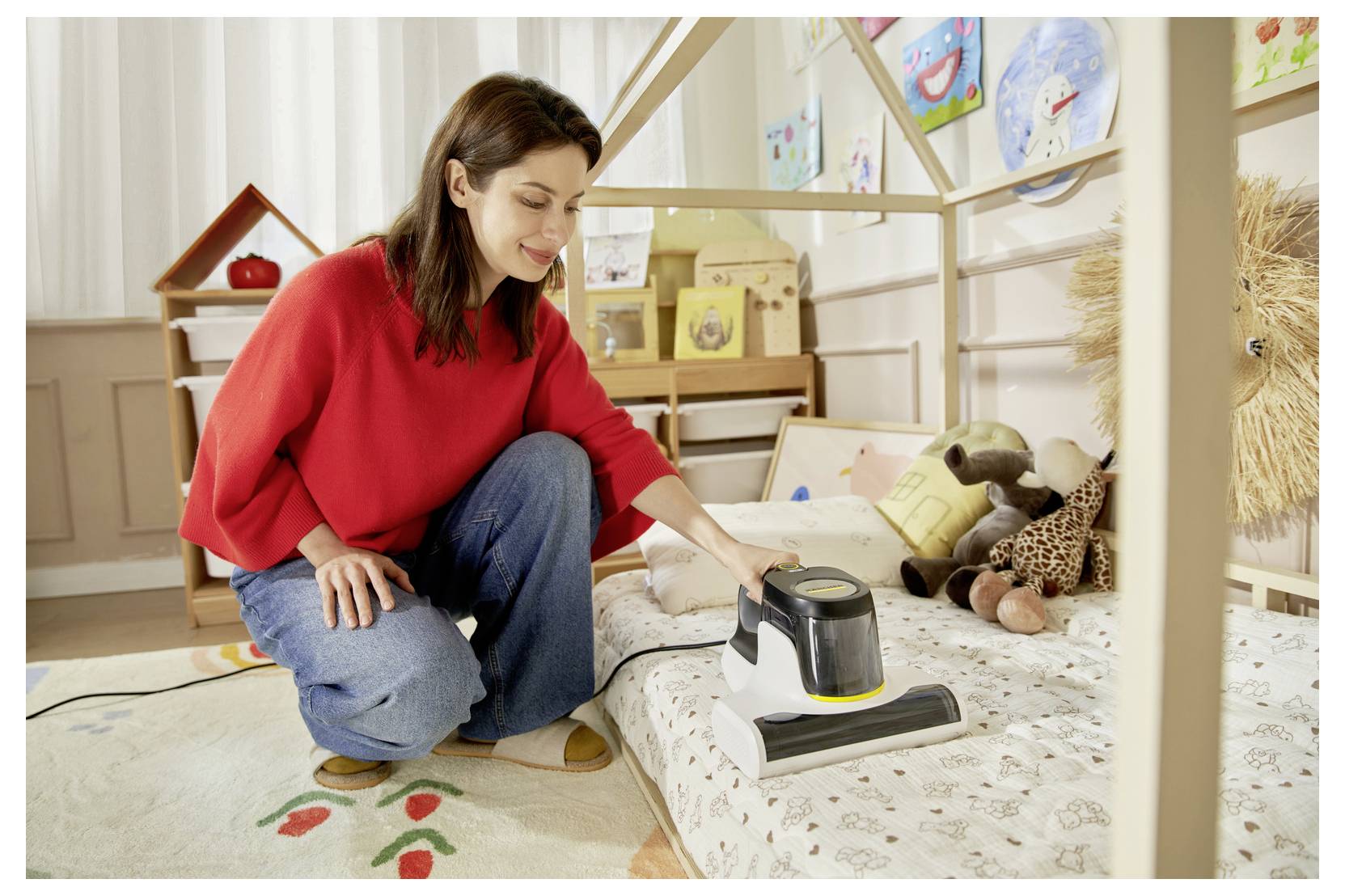 Woman vacuuming a child’s bed in a bright bedroom, with stuffed animals and playroom decor in the background.