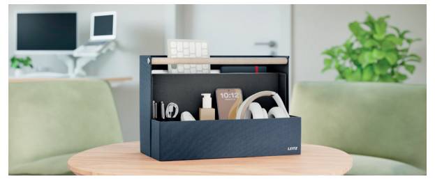 Organized desktop organizer on a round table holding headphones, books, and a phone between two sofas in a living room.