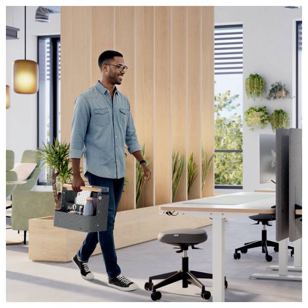 Man carries a toolbox through a modern office near desks and monitors, suggesting maintenance or setup work.<br>
