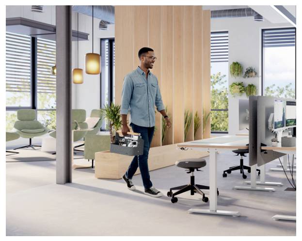 Man carrying a toolbox walks through a modern office workspace with desks, monitors, and chairs.
