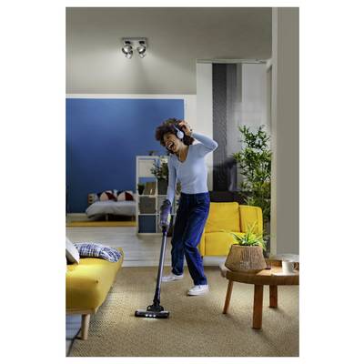 Woman vacuuming a living room while dancing, with yellow sofa, rug, plant, and coffee table in a modern home.