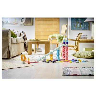 Toy cars and colorful building blocks arranged into a ramp and tower on a living room floor, with scattered play pieces around them.