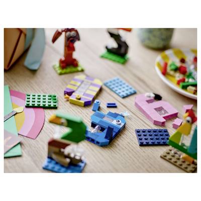 Assorted colorful LEGO pieces and small builds scattered on a wooden table, with a blue blocky toy vehicle in the center.