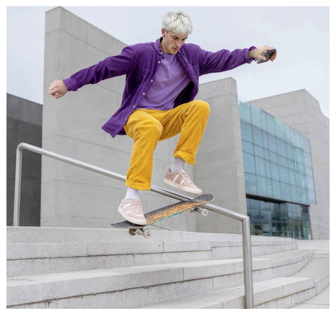 Skateboarder in purple jacket and yellow pants grinding a handrail down outdoor concrete steps by a modern building.