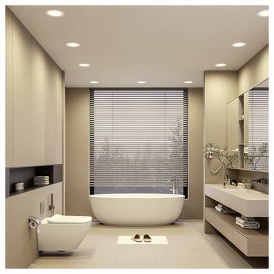 Modern beige bathroom with a freestanding tub by a window, wall-mounted toilet, vanity, and bath mat with slippers.