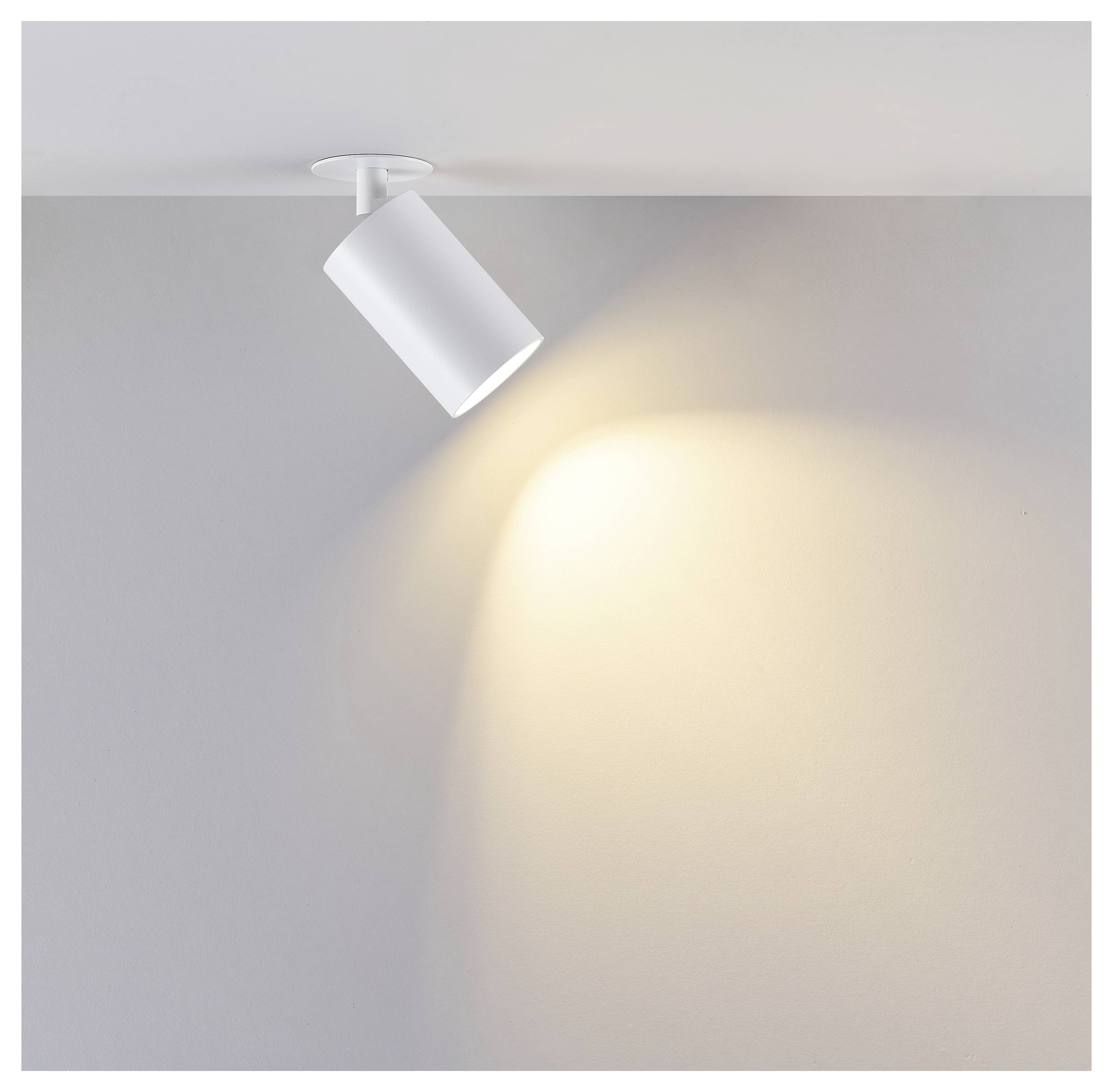 White adjustable ceiling spotlight casting a warm beam of light onto a plain gray wall.<br>