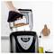 Hand removes a loaf pan of baked bread from an open bread maker in a kitchen, with oil and flour ingredients nearby.<br>