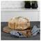 Round loaf of rustic bread on a wooden board with a blue cloth in a kitchen setting.