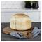 Round loaf of bread dusted with poppy seeds on a wooden cutting board, with a blue cloth on a kitchen counter<br>