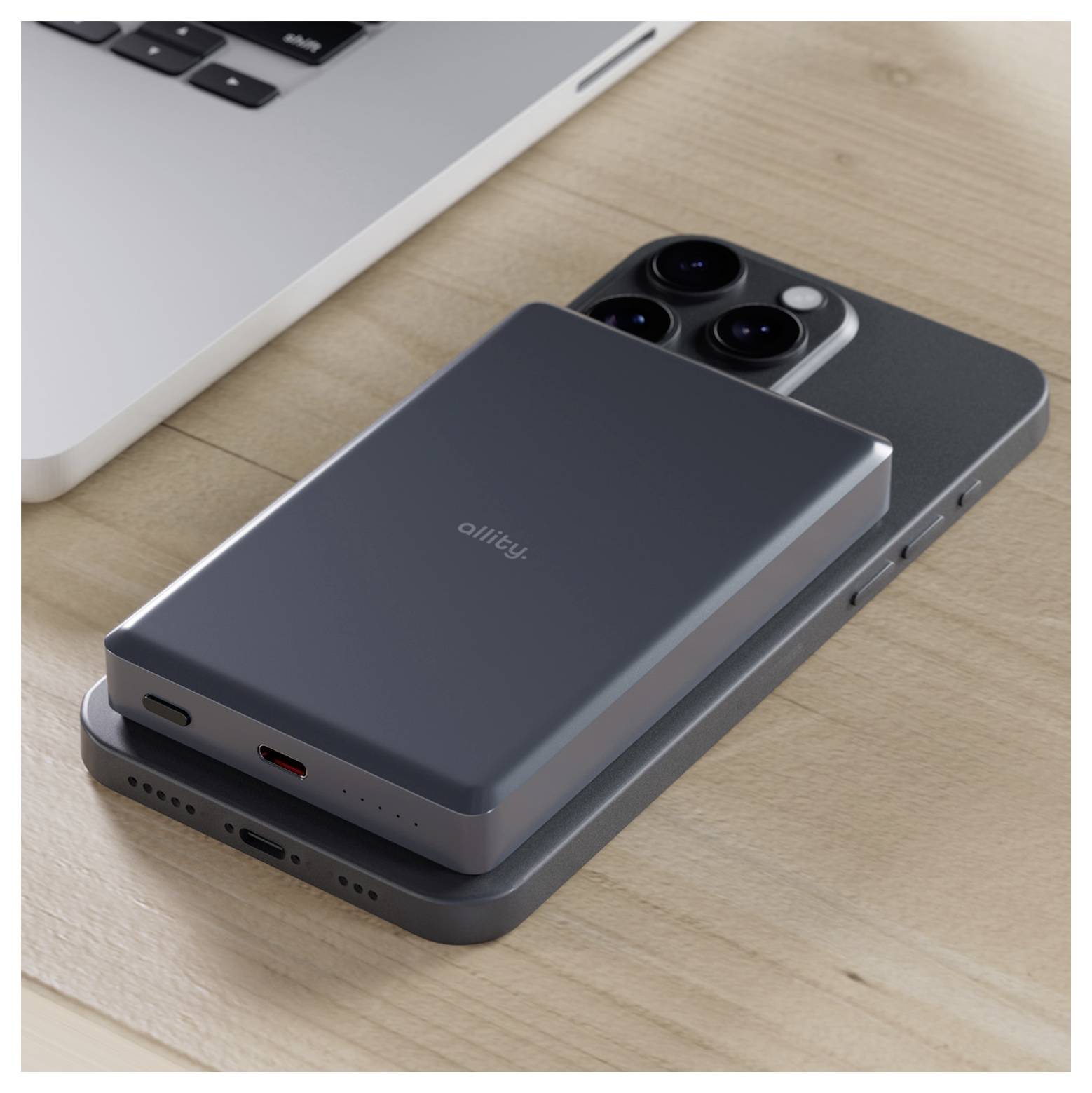 Two stacked smartphones on a desk, with a dark Anker battery pack charging the top phone beside a laptop.<br>