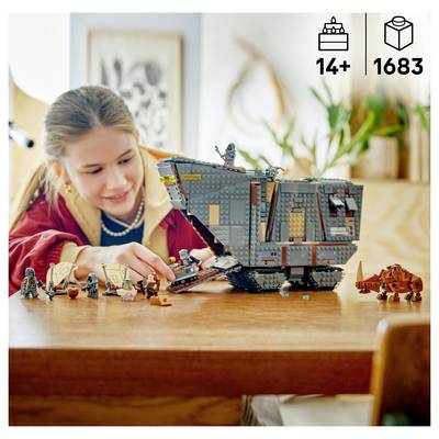 Girl plays with a large gray LEGO starship model on a table, with several small minifigures and an orange vehicle nearby.